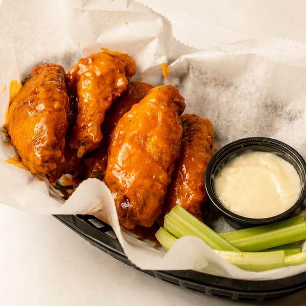 Basket of buffalo chicken wings with celery sticks and a side of ranch dressing.