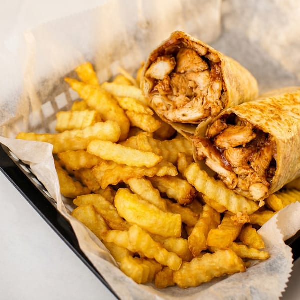 Two chicken wraps with crinkle-cut fries served in a black basket lined with white paper.